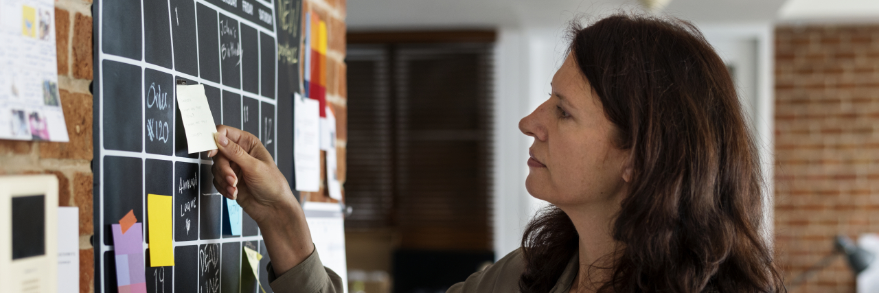 6 Tips for Addressing Executive Functioning Challenges Woman putting sticky note on calendar.