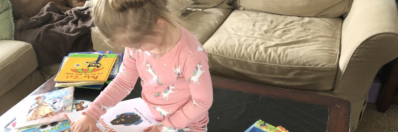 COVID-19 Pandemic Life With My Daughter With Down Syndrome A young girl is reading book and sitting on the floor.