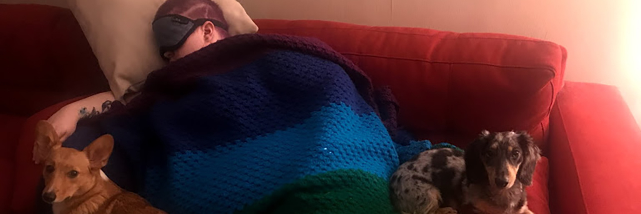 Abbi sleeping under a rainbow blanket with her dogs beside her.