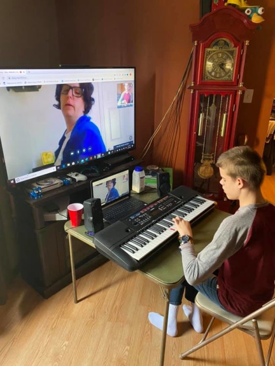 Boy with disability learning to play piano on zoom call with teacher