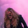 Kesha performs in a black outfit in front of pink mist