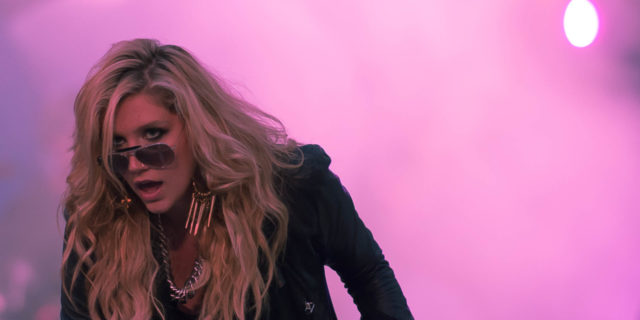 Kesha performs in a black outfit in front of pink mist