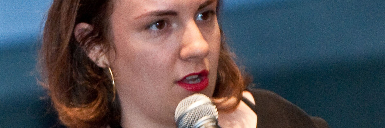 Lena Dunham in a black outfit speaks at an event