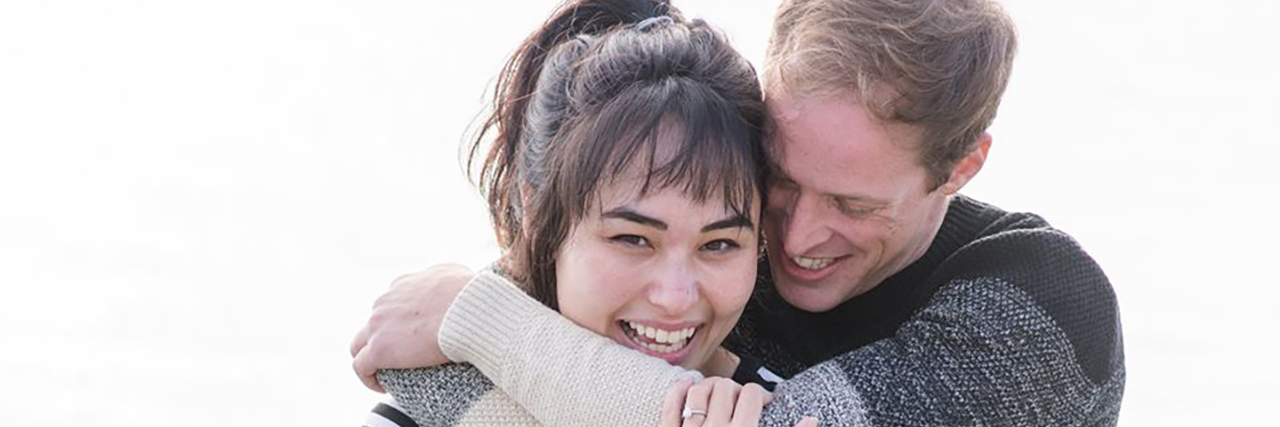 Quality-Adjusted Life Years Devalue Autistic People During COVID-19 Mickey Rowe and Helen Marion. An Asian woman with bangs and a loose pony tail smiles while in the arms of a man with light brown hair who is looking down.