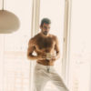 A shirtless Nyle DiMarco poses in white pants