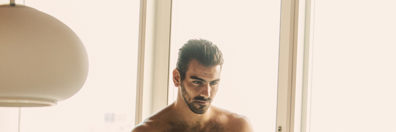 A shirtless Nyle DiMarco poses in white pants