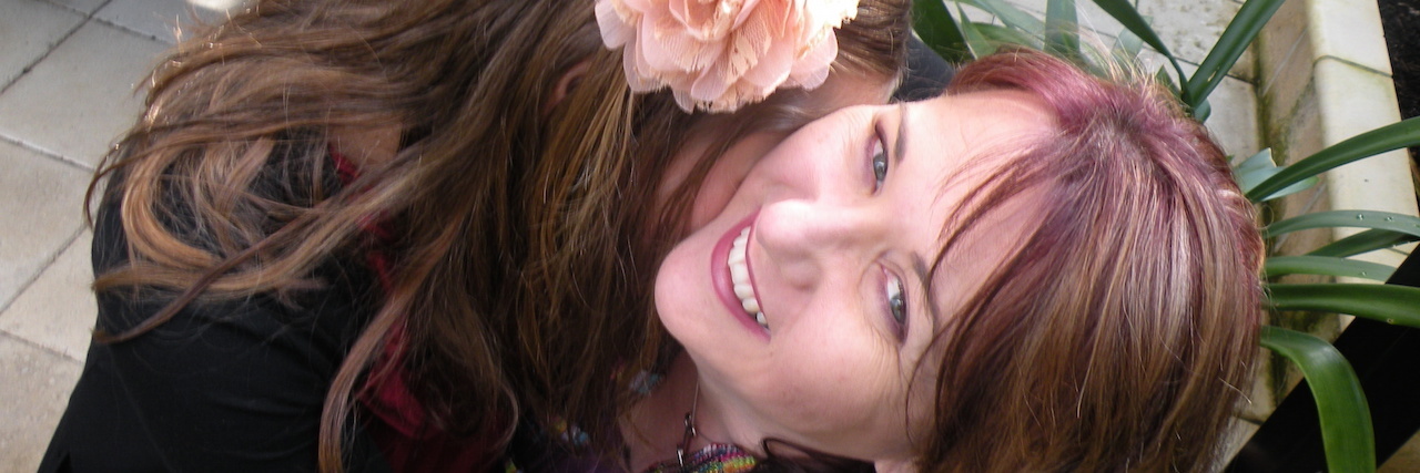 What It's Like Growing Up With My Mom Before She Died by Suicide The author and her mom, hugging. They have flowers in their hair