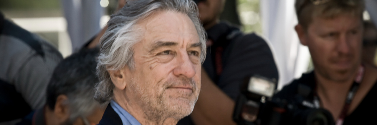 Robert De Niro looks ahead, dressed in a blue suit, on the red carpet