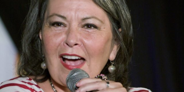Roseanne Barr in a striped shirt speaks into a microphone