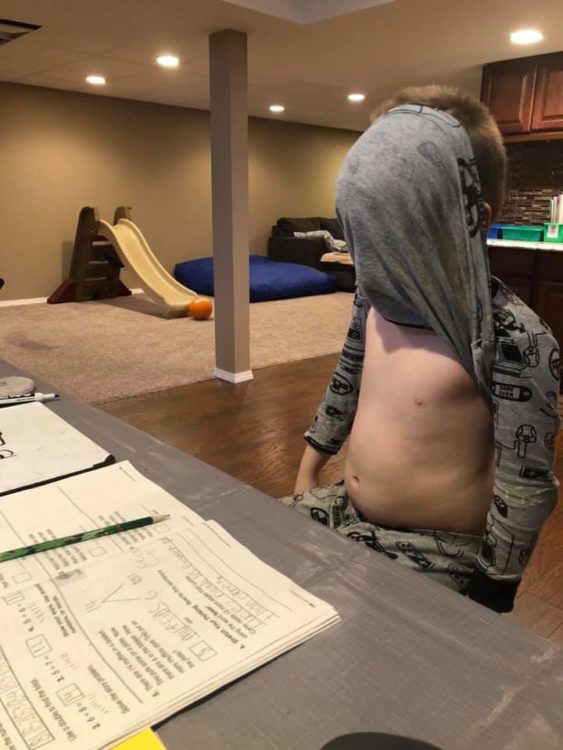 Little boy avoiding homework by hiding his face in shirt