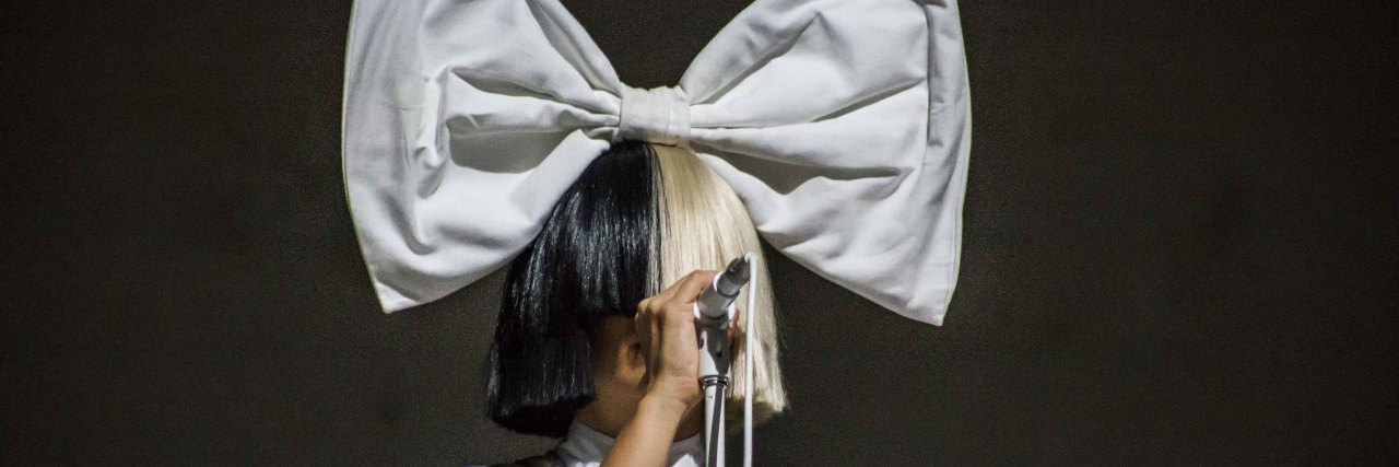 Sia singing onstage with a giant bow on her head