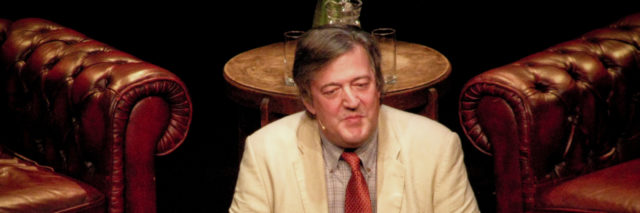 Stephen Fry speaks from a podium at the Border Kitchen in a suit