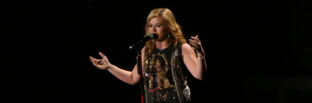 Kelly Clarkson performing onstage in a black ensemble