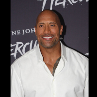 The Rock poses on the red carpet while wearing a white button-down shirt