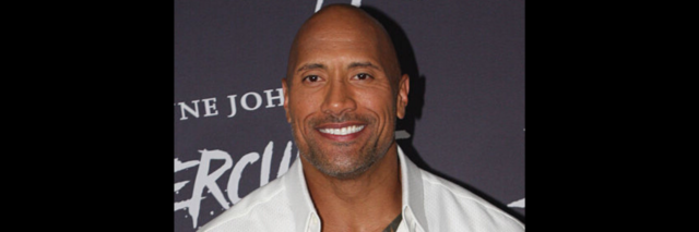 The Rock poses on the red carpet while wearing a white button-down shirt