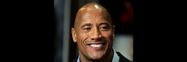 The Rock holds a microphone while wearing a suit