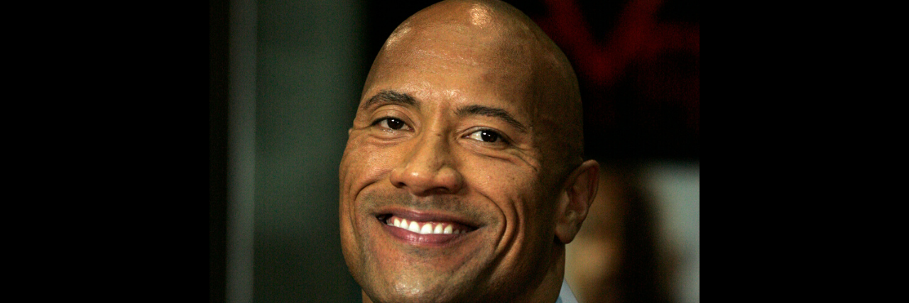 The Rock holds a microphone while wearing a suit