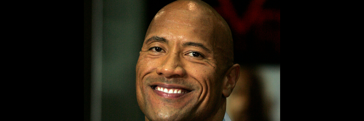 The Rock Started a Conversation About Depression on Twitter The Rock holds a microphone while wearing a suit