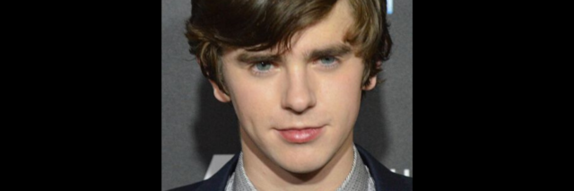 Freddie Highmore stands on the red carpet in a suit
