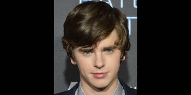 Freddie Highmore stands on the red carpet in a suit