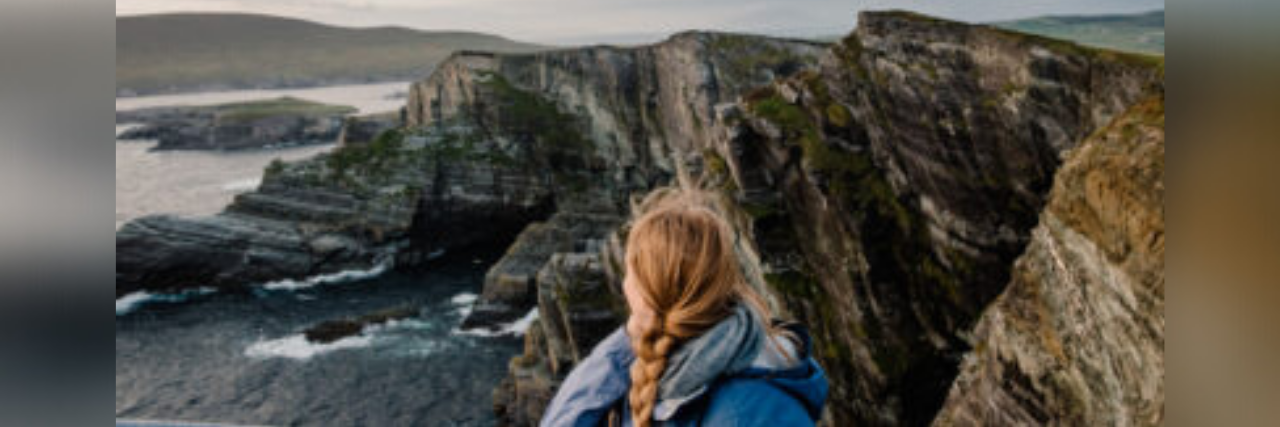 5 Surprising Things I've Learned From Living With Chronic Illness back of author sitting on a cliff in Ireland overlooking water and rocks
