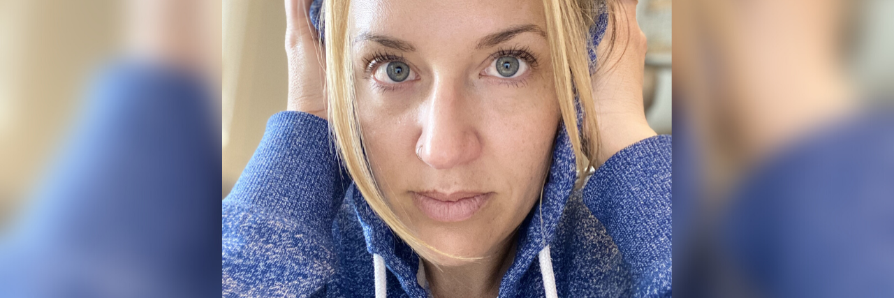 photo of contributor with blonde hair and sweating hooded sweatshirt, looking into camera with her hands over her ears