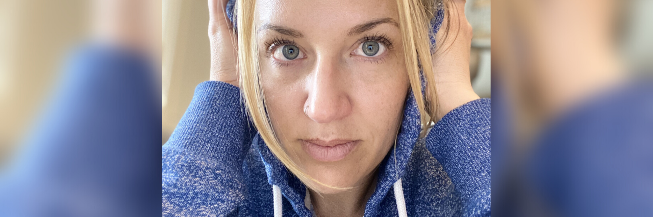 When You’re Struggling With Noise During COVID-19 Quarantine photo of contributor with blonde hair and sweating hooded sweatshirt, looking into camera with her hands over her ears