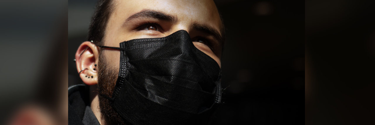 What to Know If You Have Anxiety About Life After COVID-19 photo of man wearing black face mask and looking up into sunlight