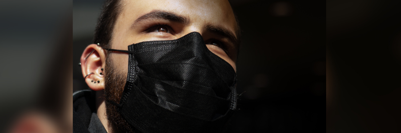 photo of man wearing black face mask and looking up into sunlight