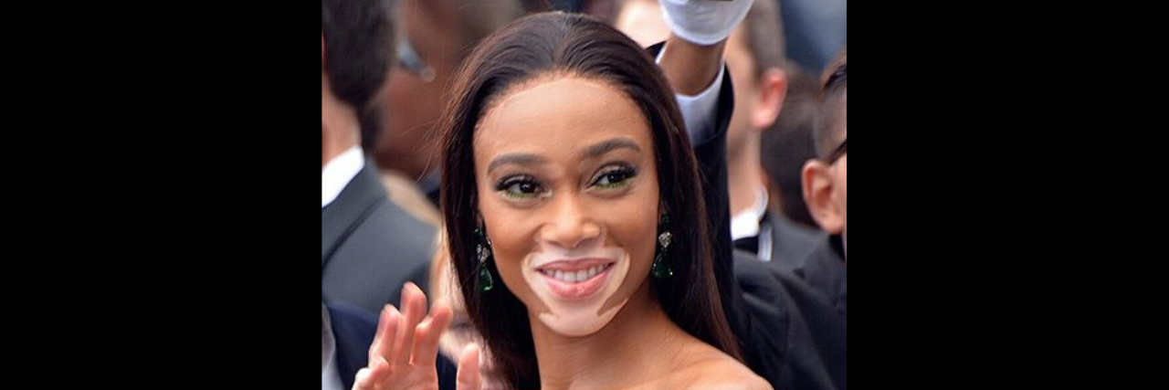 Winnie Harlow waves to the crowd in a green dress