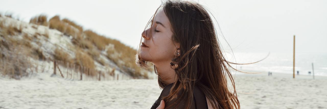 3 Ways to be Self-Aware and Present During COVID-19 Isolation woman sitting on the beach with her eyes closed, hugging herself