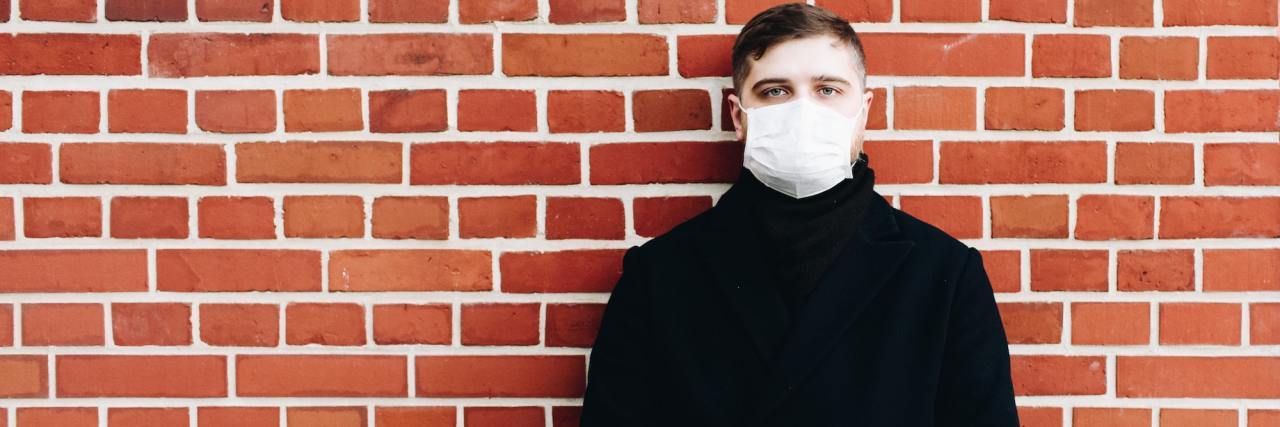 Man wearing face mask standing in front of brick wall