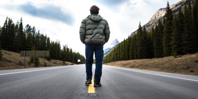 man in a winter jacket and jeans standing in the middle of a road with his back to the camera