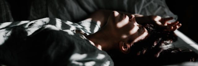 woman lying in bed with the shades reflecting over her