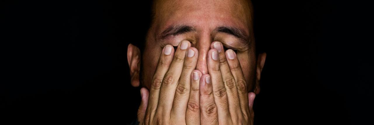 5 Reasons COVID-19 Makes Your Emotions Feel Out of Control White man wearing a plaid shirt with bird tattoos on his hands, which are covering his face