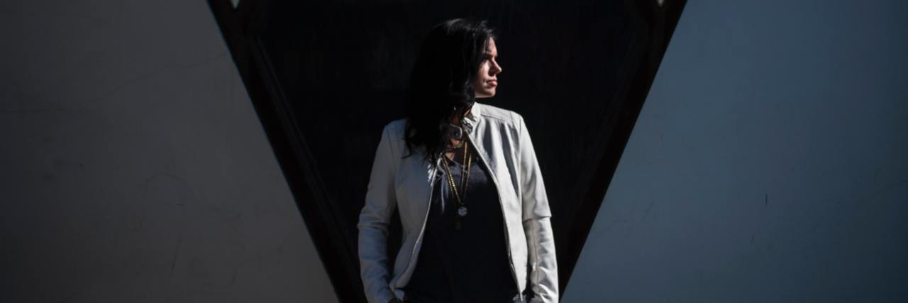 woman in a white jacket standing in front of a geometric building looking away