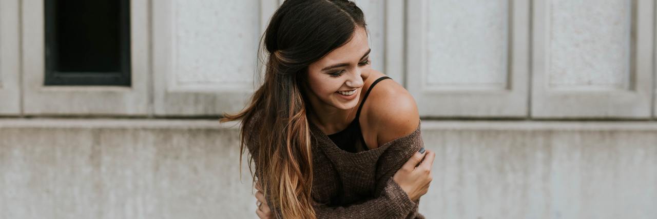 photo of young woman with arms around herself, laughing