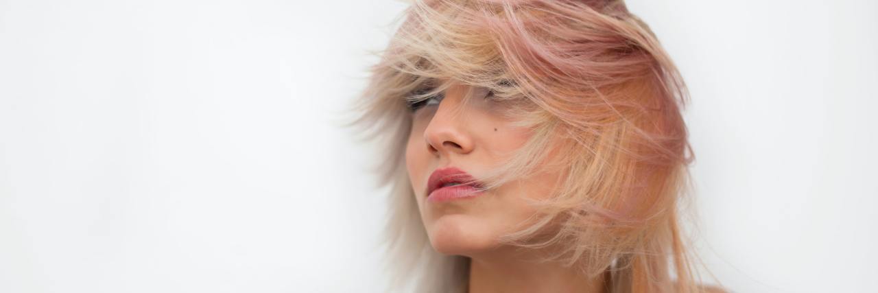 8 Symptoms of PTSD We Don't Talk About but Need to girl with pink hair blowing across her face looking away