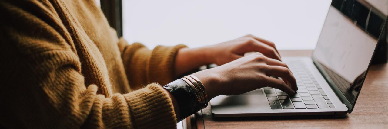 Online Classes During COVID-19 May Help Students With Mental Illness woman in a yellow sweater typing on a laptop next to a window