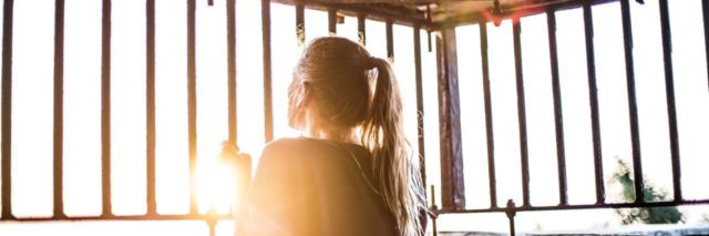 young woman holding onto bars looking outside with the sun shining
