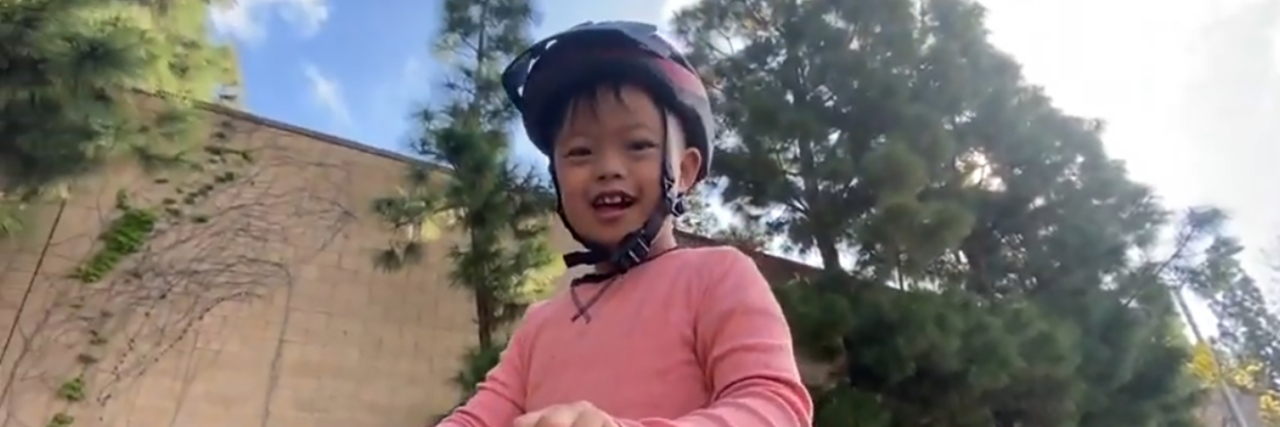 Explaining the Coronavirus Pandemic to Kids With Disabilities Boy with Down syndrome riding a kick scooter.