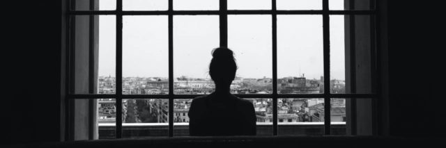 black and white photo of a woman looking out at a city through a window