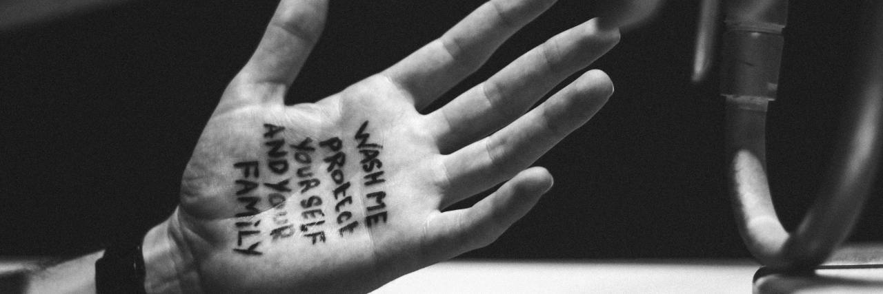 black and white photo of person washing hands with the words "wash me protect yourself and your family" written on one in pen
