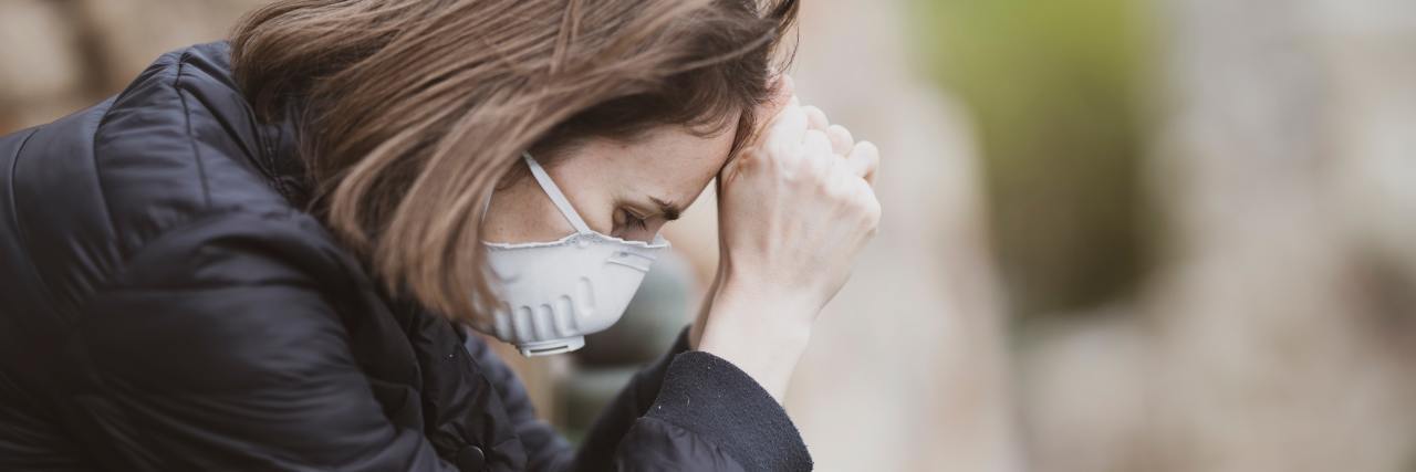Suicidal Thoughts Are a Typical Reaction to the Coronavirus Pandemic photo of woman resting forehead on hands, wearing a face mask