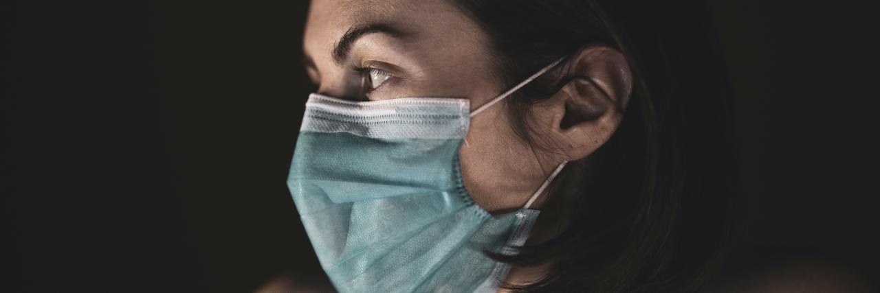photo of woman wearing blue face mask looking off to side with sadness