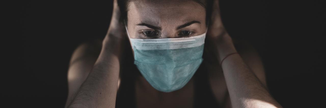 Things Making Your Mental Health Worse During COVID-19 photo of woman wearing mask looking distressed with hands at either side of her head