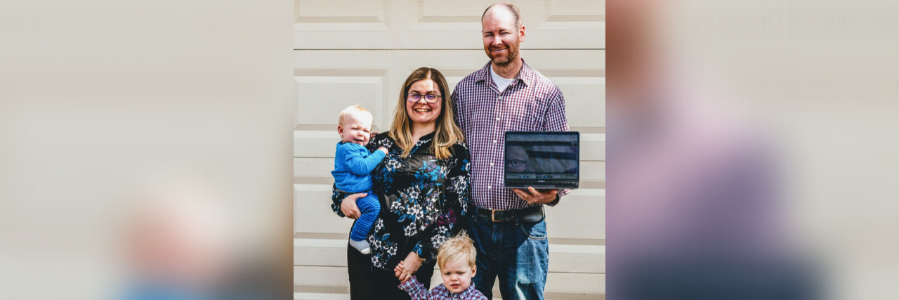 Two parents and two kids, holding a photo of their other son on a tablet