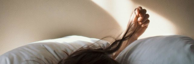photo showing light coming through window onto bed, where a girl is waking up and playing with her hair. only her hair and hand can be seen