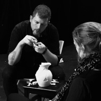 black and white photo of artist assembling a broken pitcher or jug