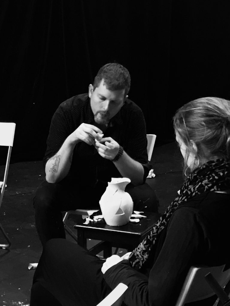 black and white photo of artist assembling a broken pitcher or jug